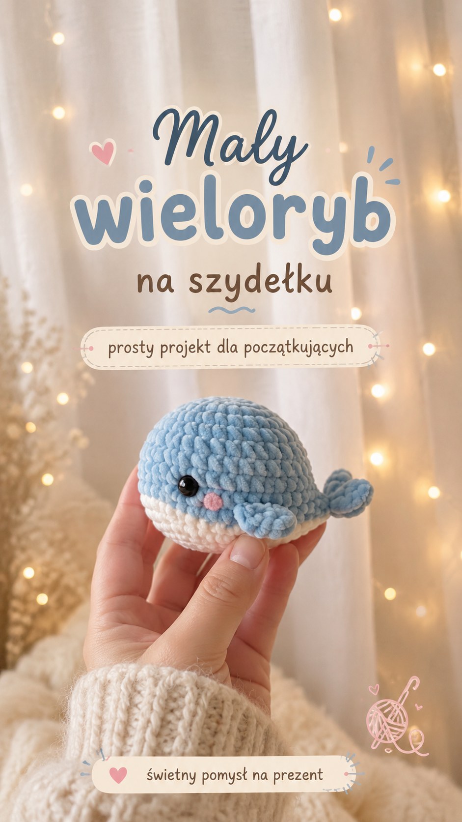 Mały szydełkowy wieloryb w kolorze niebieskim i białym trzymany w dłoni na tle świątecznych światełek